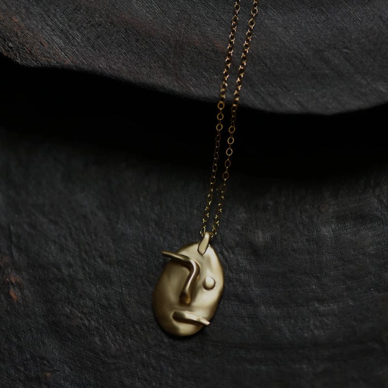 Gold face pendant necklace on dark surface.