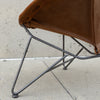 Close-up of a brown leather chair with a dark gray metal frame, set against a concrete wall and floor.