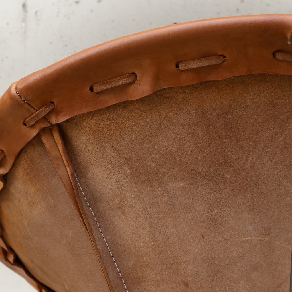 Close-up of a brown leather drum head with a stitched edge and eyelet holes, photographed against a light neutral background.