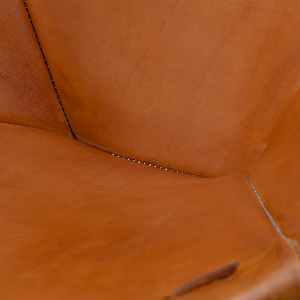 Close-up of warm tan leather upholstery with visible stitching and a small metal rivet along a seam.