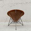 A mid-century modern spiral chair with a brown leather seat and backrest, supported by a black metal frame, photographed against a textured concrete wall.