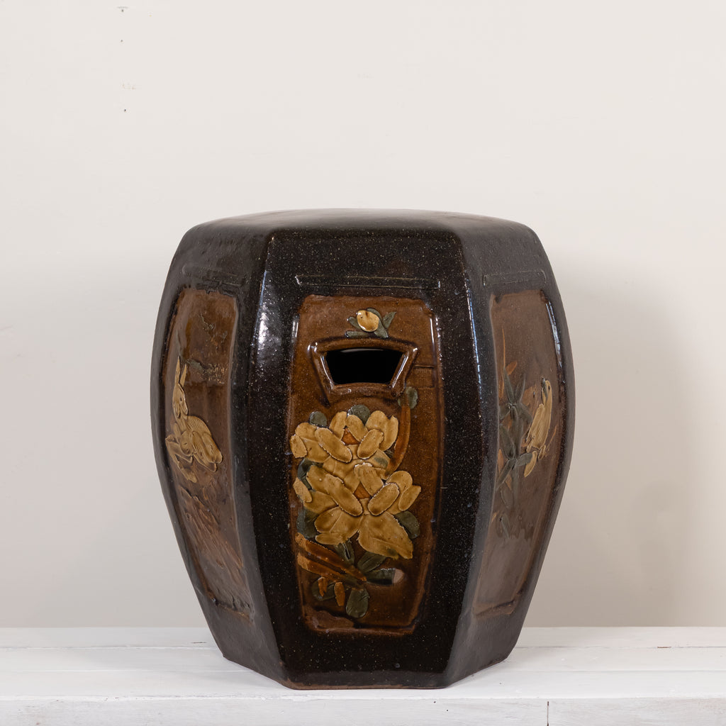 A dark brown glazed ceramic garden stool with hand-painted floral panels, photographed against a plain off-white background.