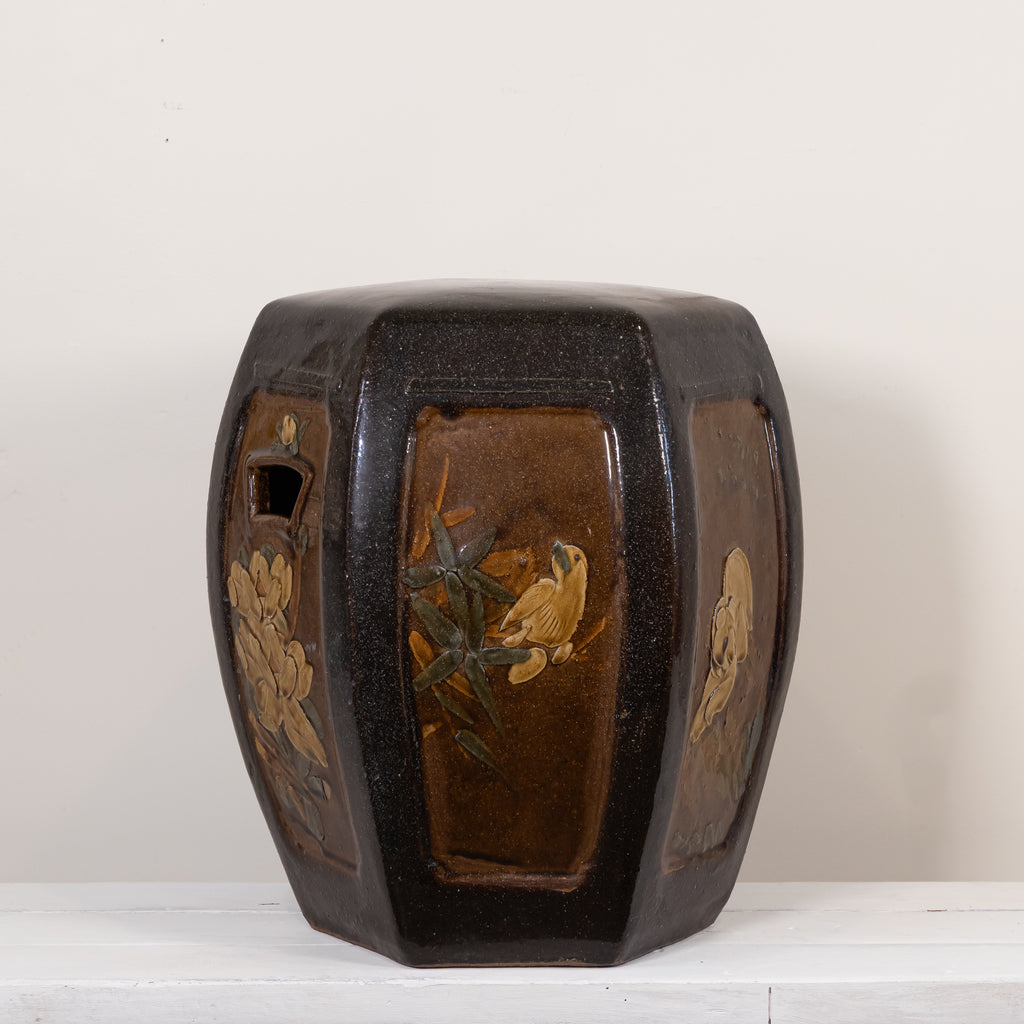 A dark brown glazed octagonal ceramic stool with hand-painted floral and bird motifs on the front panels, set against a plain off-white background.