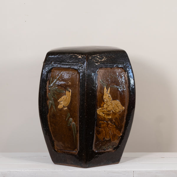 A vintage octagonal ceramic stool or box with a glossy black and brown glaze, featuring hand-painted floral and bird motifs on the front panels, set against a plain light background.