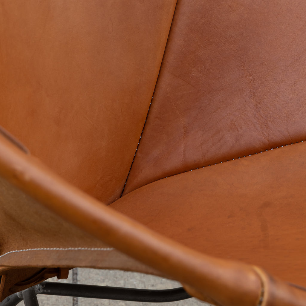 Close-up of a warm tan leather chair seat and arm with visible stitching and a small portion of a black metal frame.