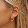 Close-up of a person wearing gold hoop earrings with blonde hair.