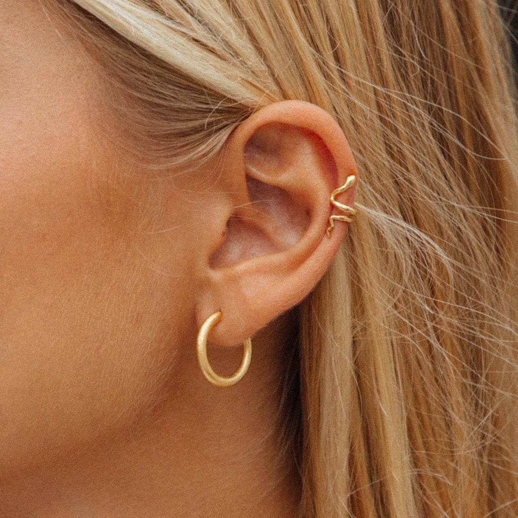 Close-up of a person wearing gold hoop earrings with blonde hair.