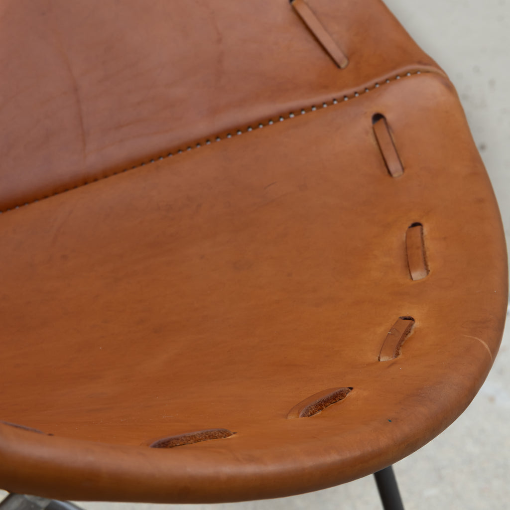 Close-up of a warm brown leather chair seat showing the texture, stitching, and seat hole construction.