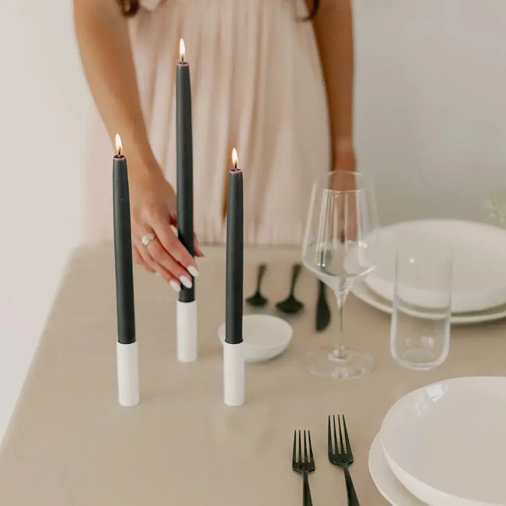 Woman holding lit black candles on a table setting.
