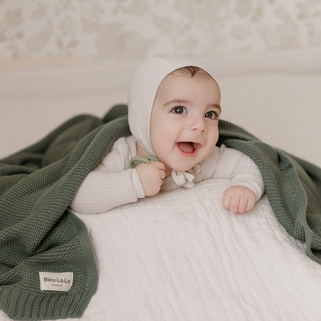Baby wrapped in a green blanket with a visible brand label on a neutral background