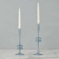 Two light blue glass candle holders with white candles on a gray background