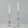 Two light blue glass candle holders with white candles on a gray background