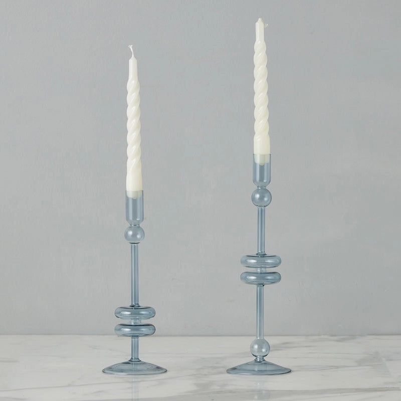 Two light blue glass candle holders with white candles on a gray background