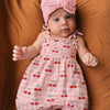 Baby wearing a pink romper with cherry pattern and matching headband on a brown background