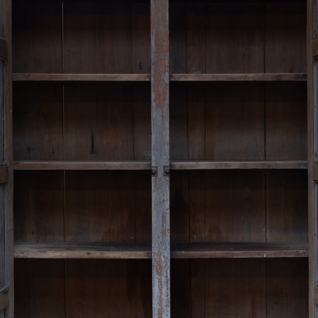 An empty rustic wooden bookcase with four shelves and weathered brown panels, shown from the front with the center door panel slightly open.