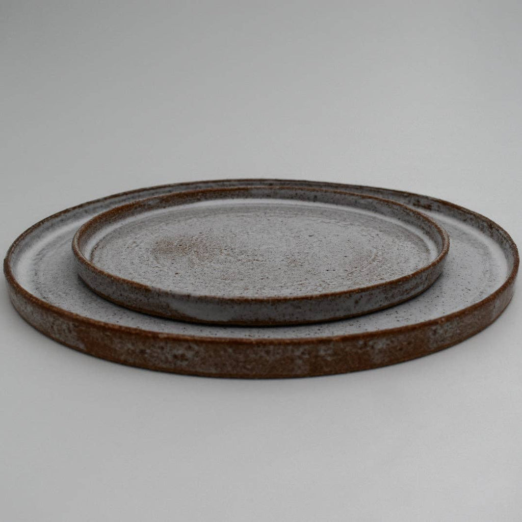 Two round ceramic plates with a rustic finish on a light gray background