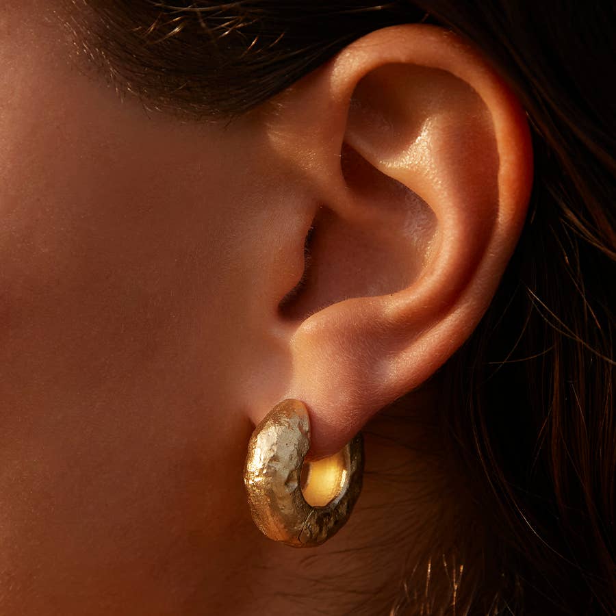 Close-up of an ear wearing a gold earring with a textured design.