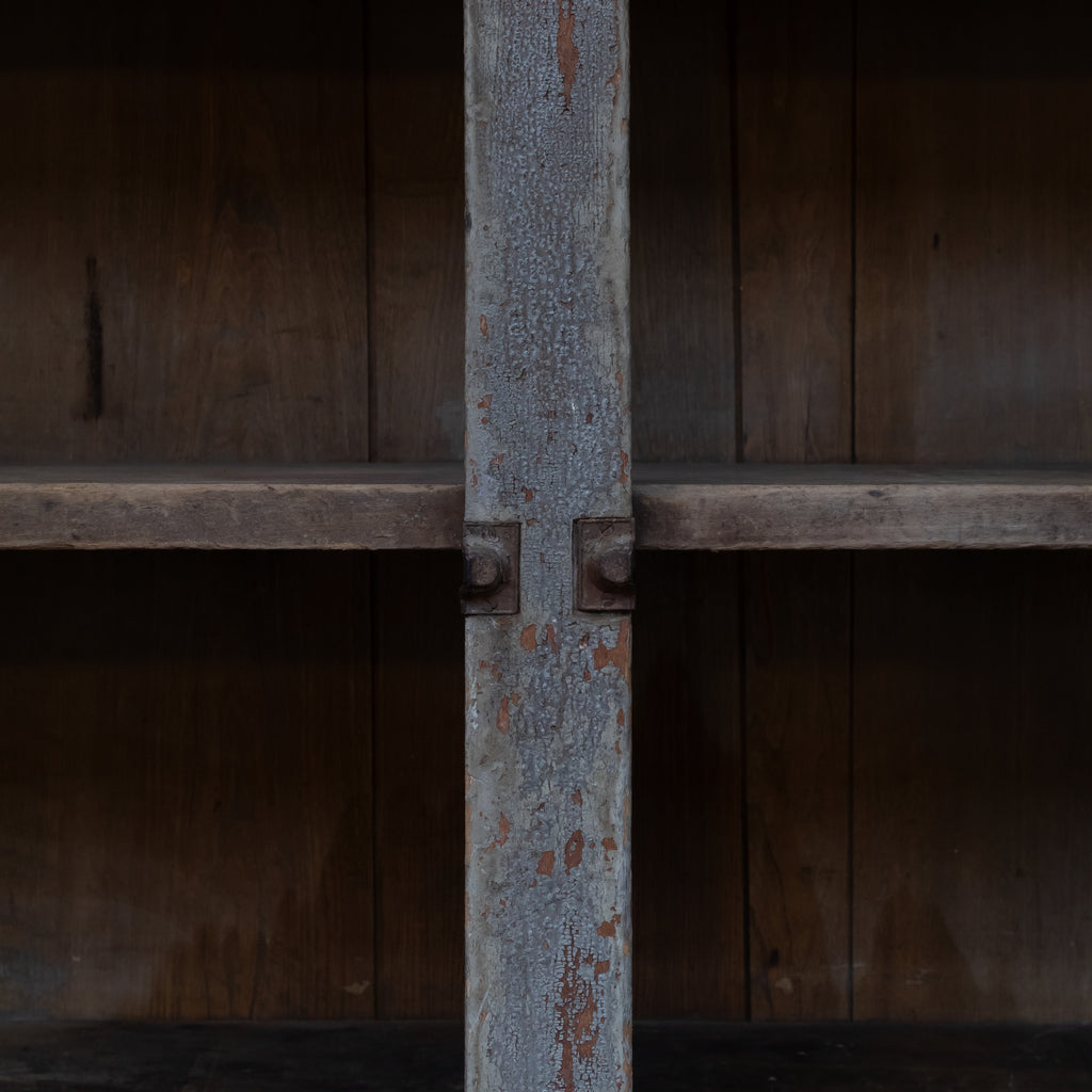 Close-up of a rustic wooden shelving unit with a central painted support post showing peeling gray paint and weathered metal brackets against dark wood shelves.