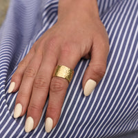 Hand with gold ring on a blue and white striped fabric background