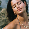 Woman with gold hoop earrings and necklace against a natural background