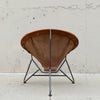 A mid-century modern spiral chair with a brown leather seat and backrest, supported by a black metal frame, photographed against a concrete wall.