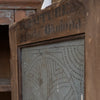 Close-up of a vintage wooden cabinet or screen with a metal patterned panel and stenciled text reading 'FURNITURE Liberty " Okolona"' on the top frame.