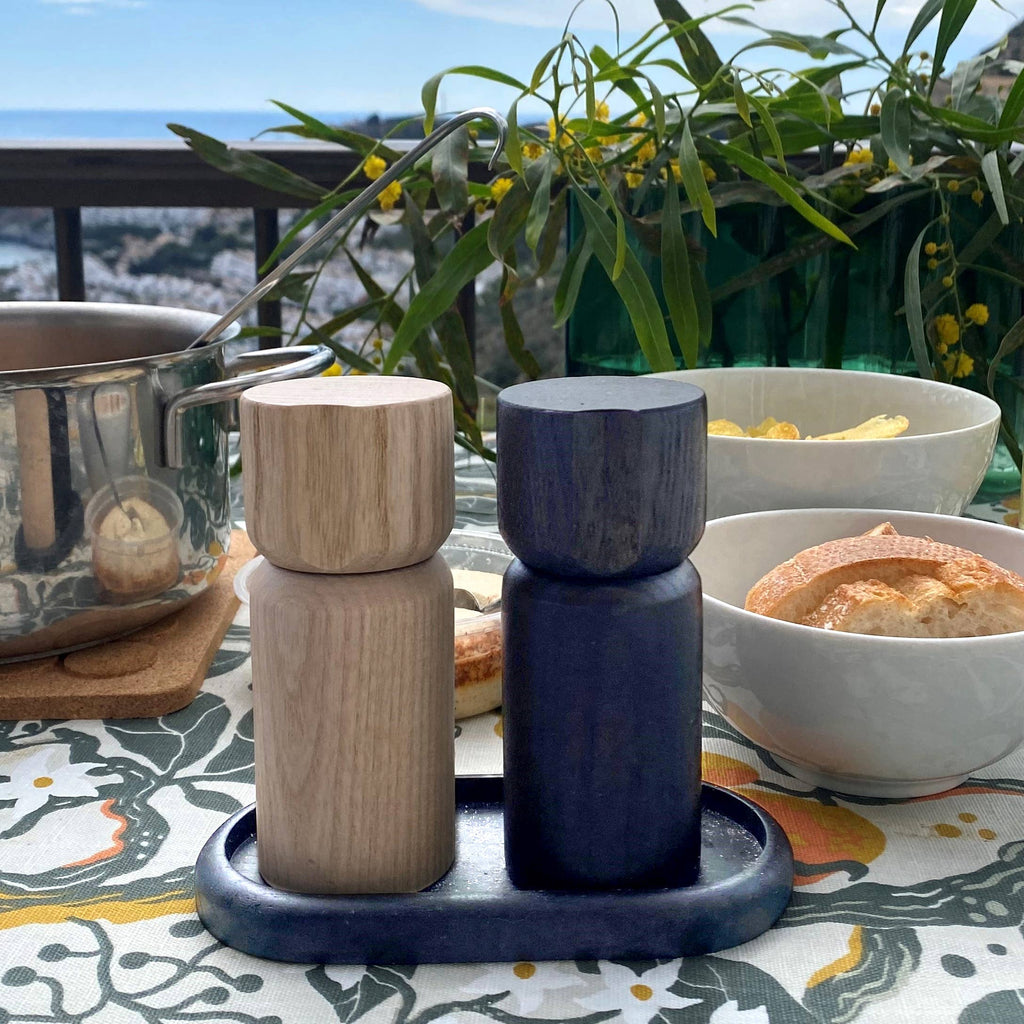 Two wooden salt and pepper grinders on a tray, with bowls of food.