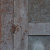 Close-up of weathered gray wooden panels with peeling paint and a small metal hinge, alongside textured gray metal sections.