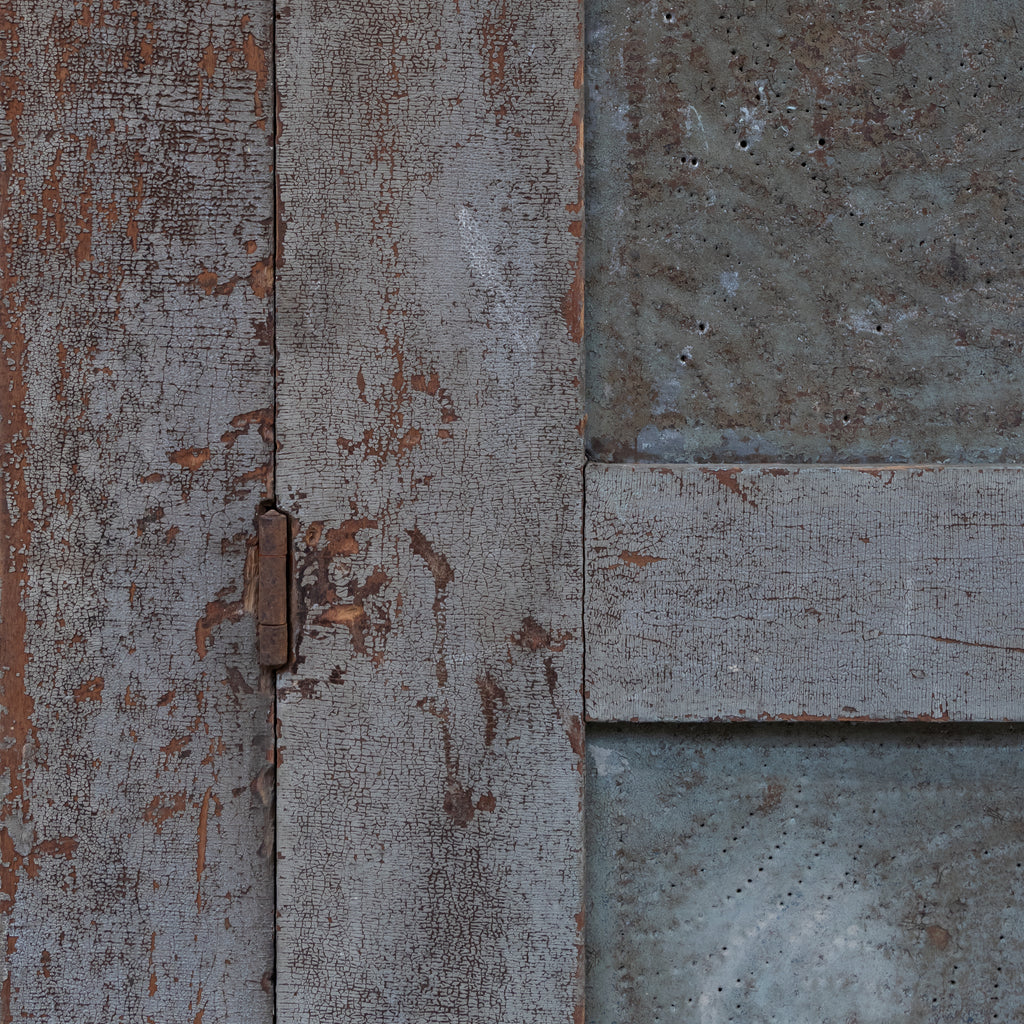 Close-up of weathered gray wooden panels with peeling paint and a small metal hinge, alongside textured gray metal sections.