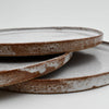 Three ceramic plates with a rustic finish stacked on a white background