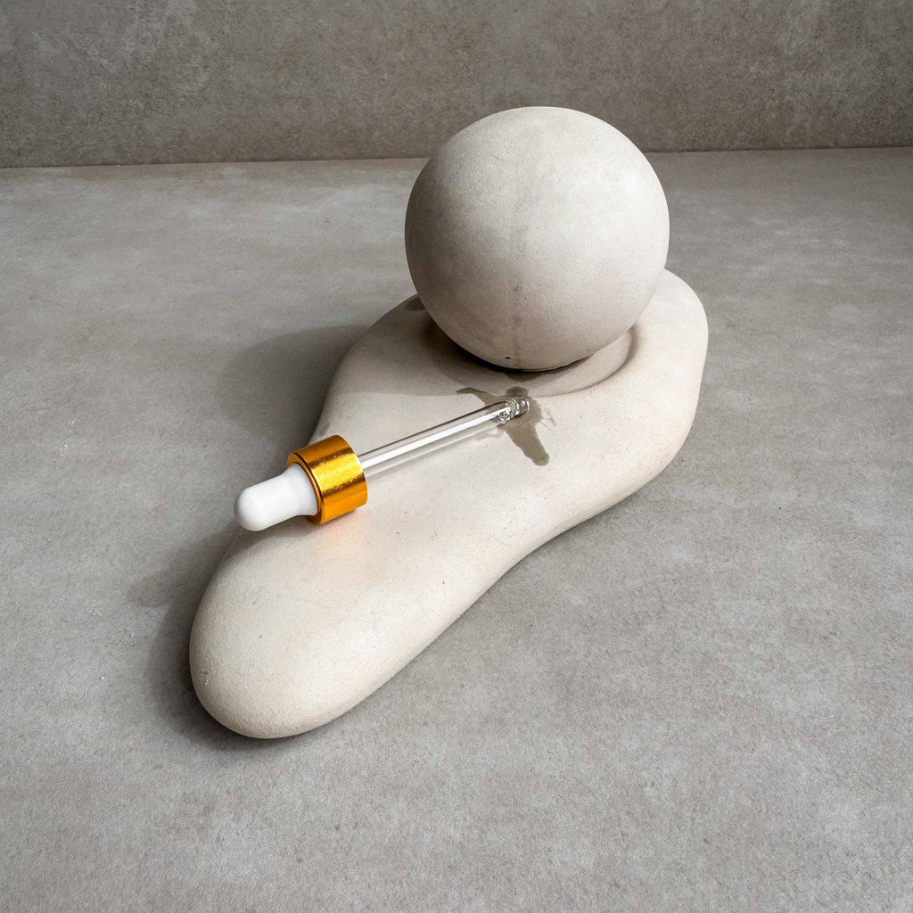 Ceramic dropper bottle with gold cap on a stone surface