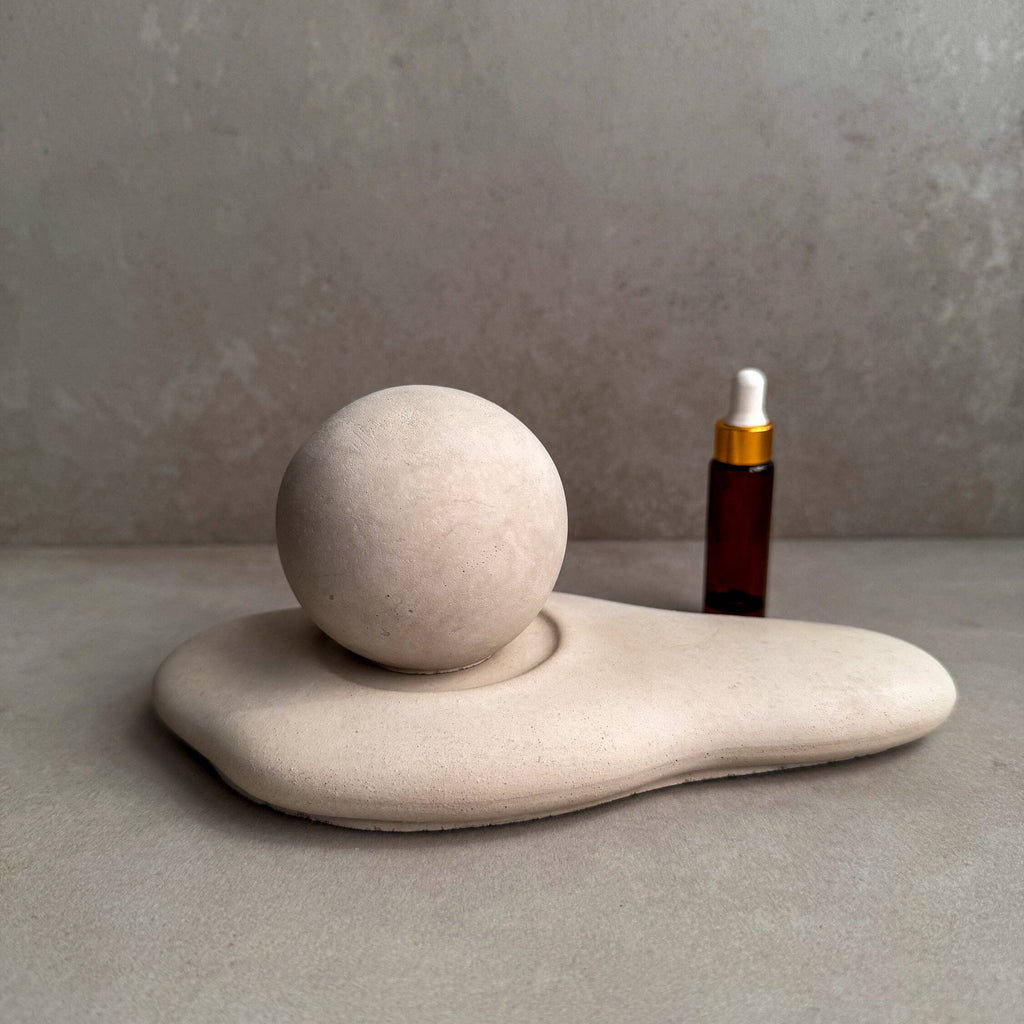 Ceramic sculpture with a sphere and a dropper bottle on a gray surface