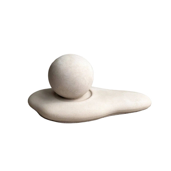 Abstract sculptural decor piece featuring a smooth matte sphere resting on an organic, fluid base, set against a textured concrete background.