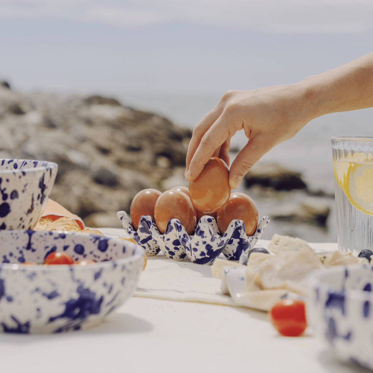 Person placing eggs into a decorative egg holder on a table with bowls and a glass of water.
