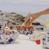 Person placing eggs into a decorative egg holder on a table with bowls and a glass of water.