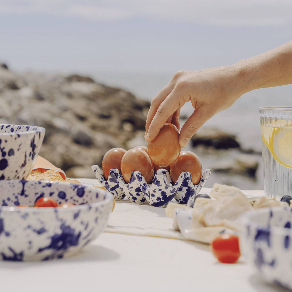 Person placing eggs into a decorative egg holder on a table with bowls and a glass of water.