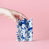 Hand holding a blue and white ceramic pouch against a pink background