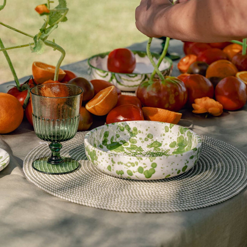 Table setting with patterned bowls and glasses surrounded by fruits on a natural background