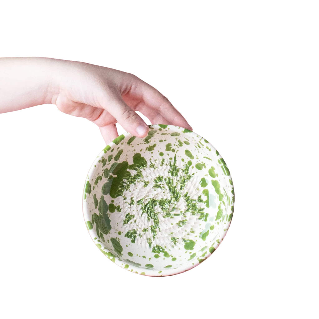Hand holding a green and white patterned bowl against a pink background