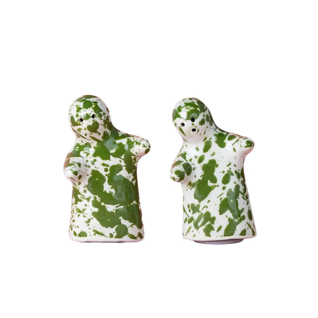 Two small ceramic salt and pepper figurines with a green and white splatter pattern, standing side by side on a solid pink background