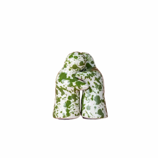 A salt and pepper shaker set with a white and green paint splatter pattern, shown from the back on a solid pink background.