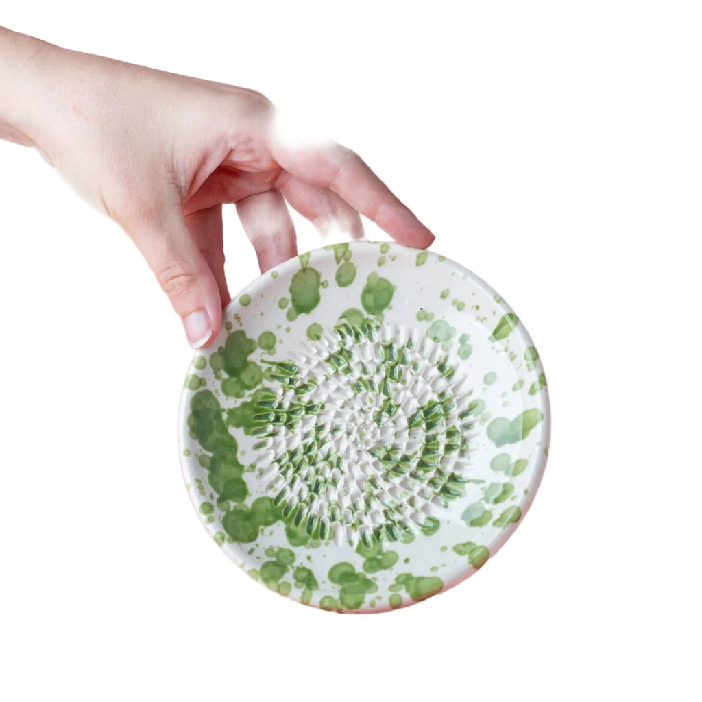 Hand holding a green and white patterned ceramic plate against a pink background