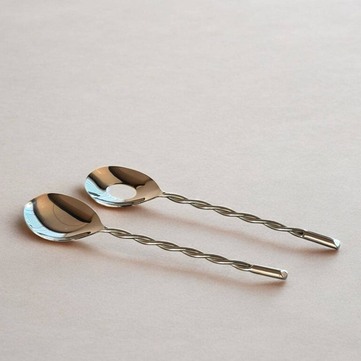 Two silver spoons with twisted handles on a light pink background