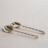 Two silver spoons with twisted handles on a light pink background