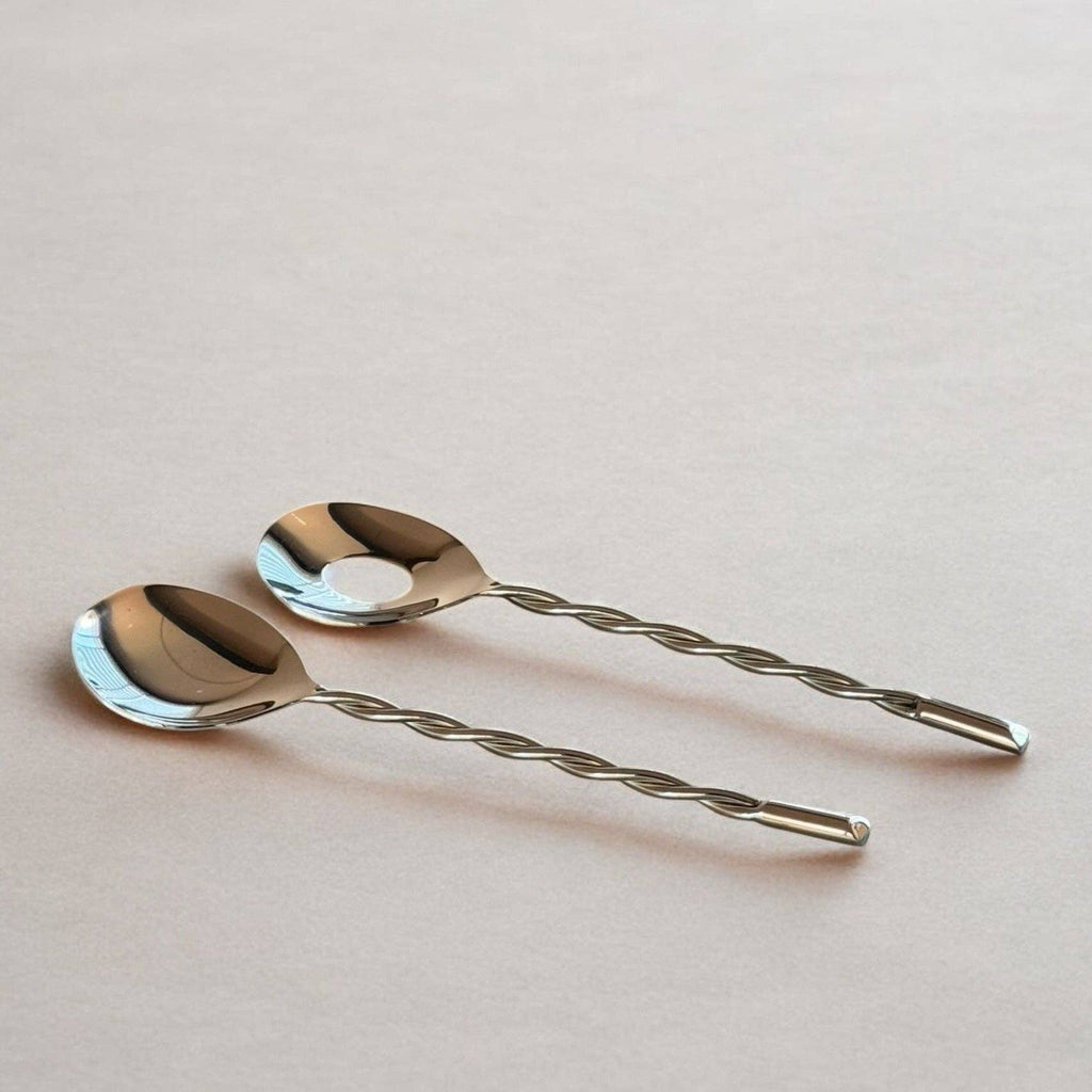 Two silver spoons with twisted handles on a light pink background
