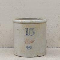 An antique 15 oz stoneware crockery jar with a distressed off-white glaze, featuring a blue printed number 15, a brown wing graphic, and a blue circular stamp reading 'New Orleans Co. 1870'.
