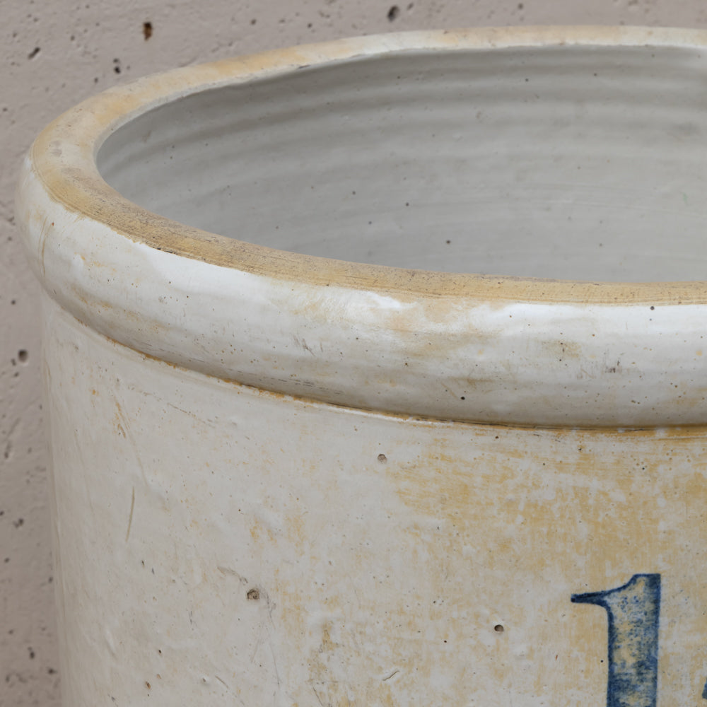 Close-up of a large ceramic pot or planter with a distressed off-white glaze, showing a blue painted number '1' near the bottom right and a natural clay rim.