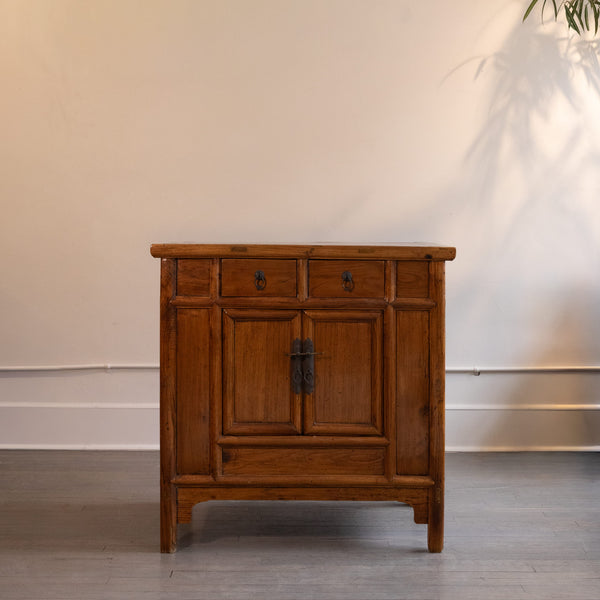 Antique Chinese cabinet with two doors and two drawers against a plain wall.