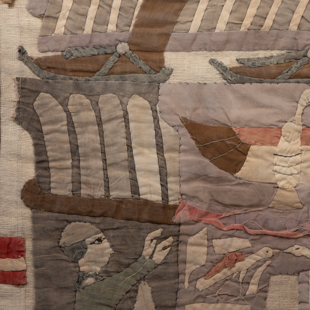 A close-up of a vintage patchwork quilt featuring stitched scenes of sailing ships, a lighthouse, and a sailor in muted tones of beige, brown, gray, and dusty pink.