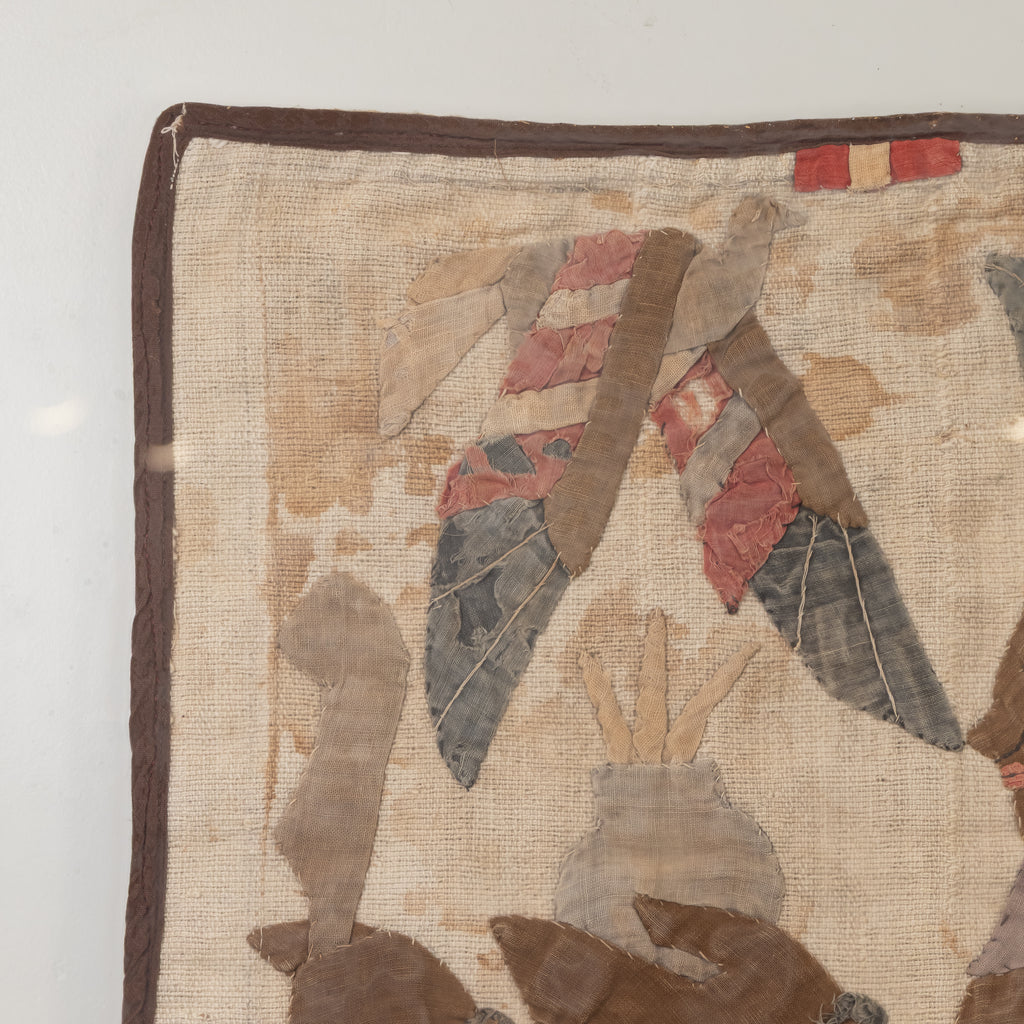 A close-up of a vintage patchwork quilt showing a beige linen base with brown borders and various fabric patches in muted tones of red, gray, and brown.